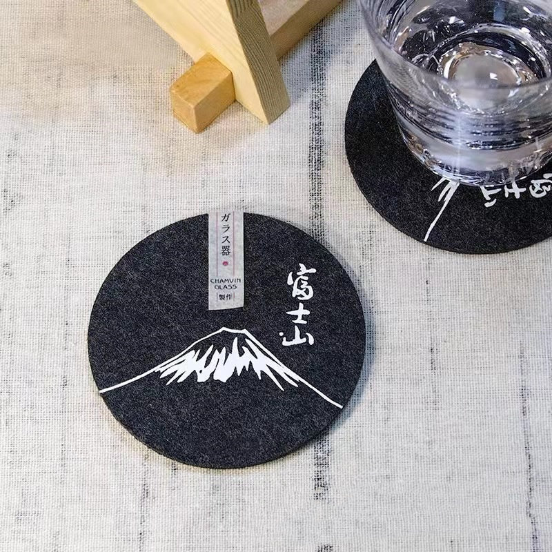 Set of eight round black felt coasters arranged on a wooden table surface.