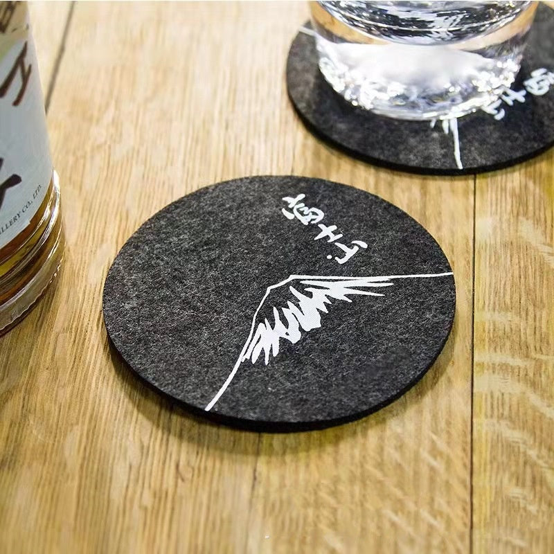 Set of eight round black felt coasters arranged on a wooden table surface.